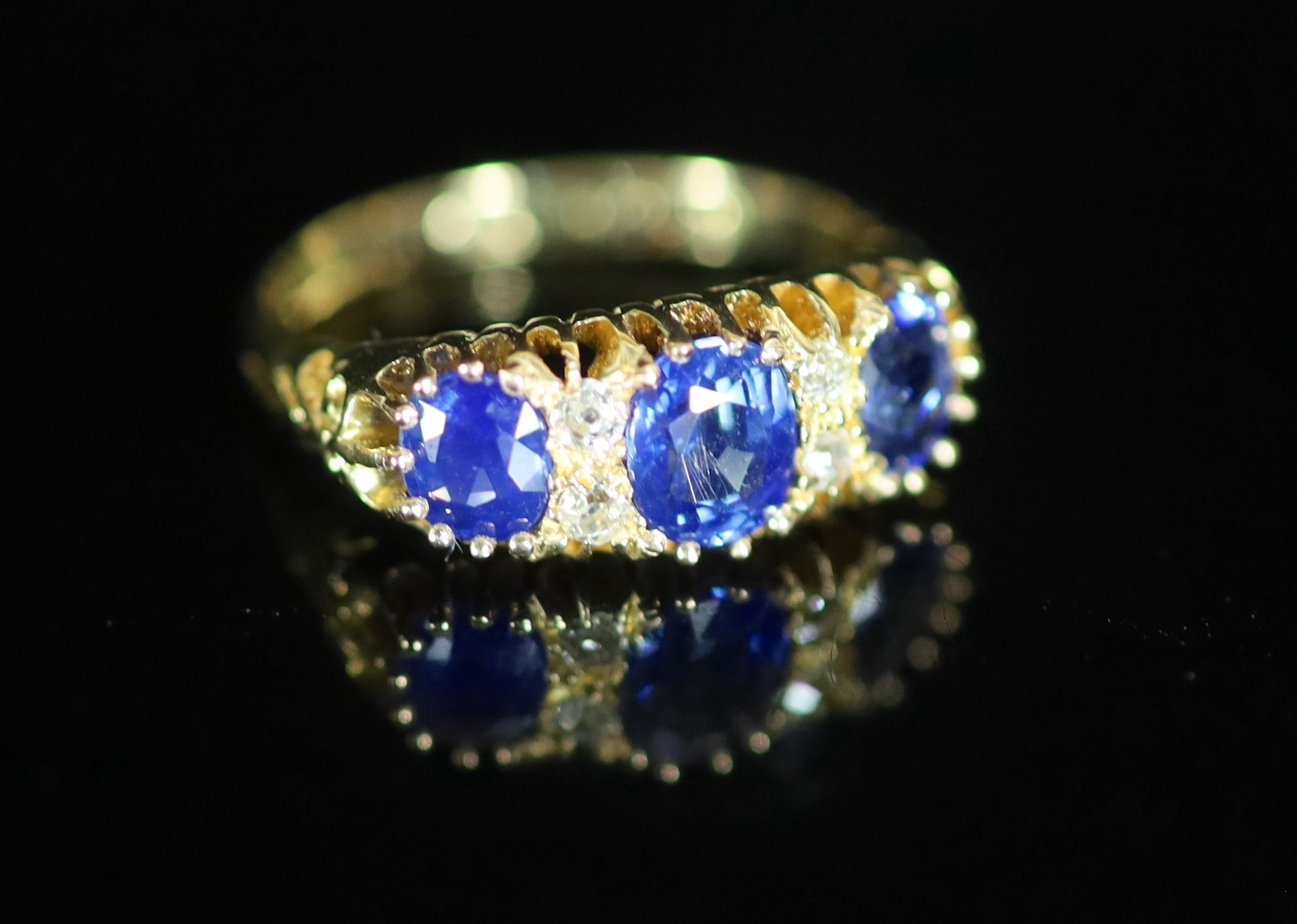 An Edwardian 18ct gold and three stone sapphire set half hoop ring with diamond chip spacers